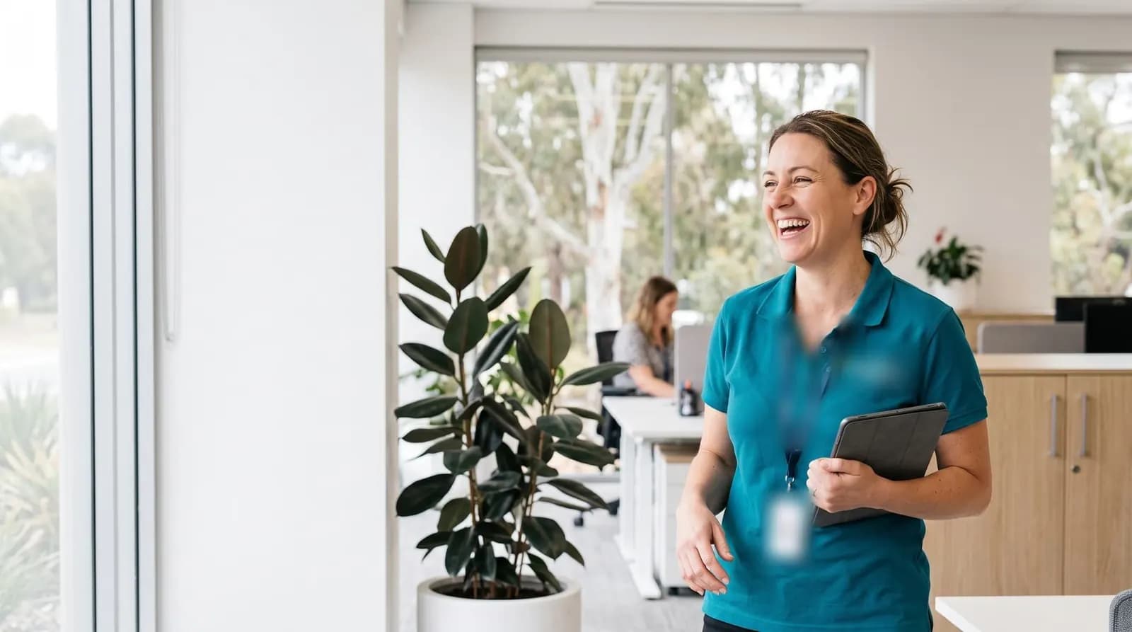 A smiling coordinator holding a tablet in a bright office