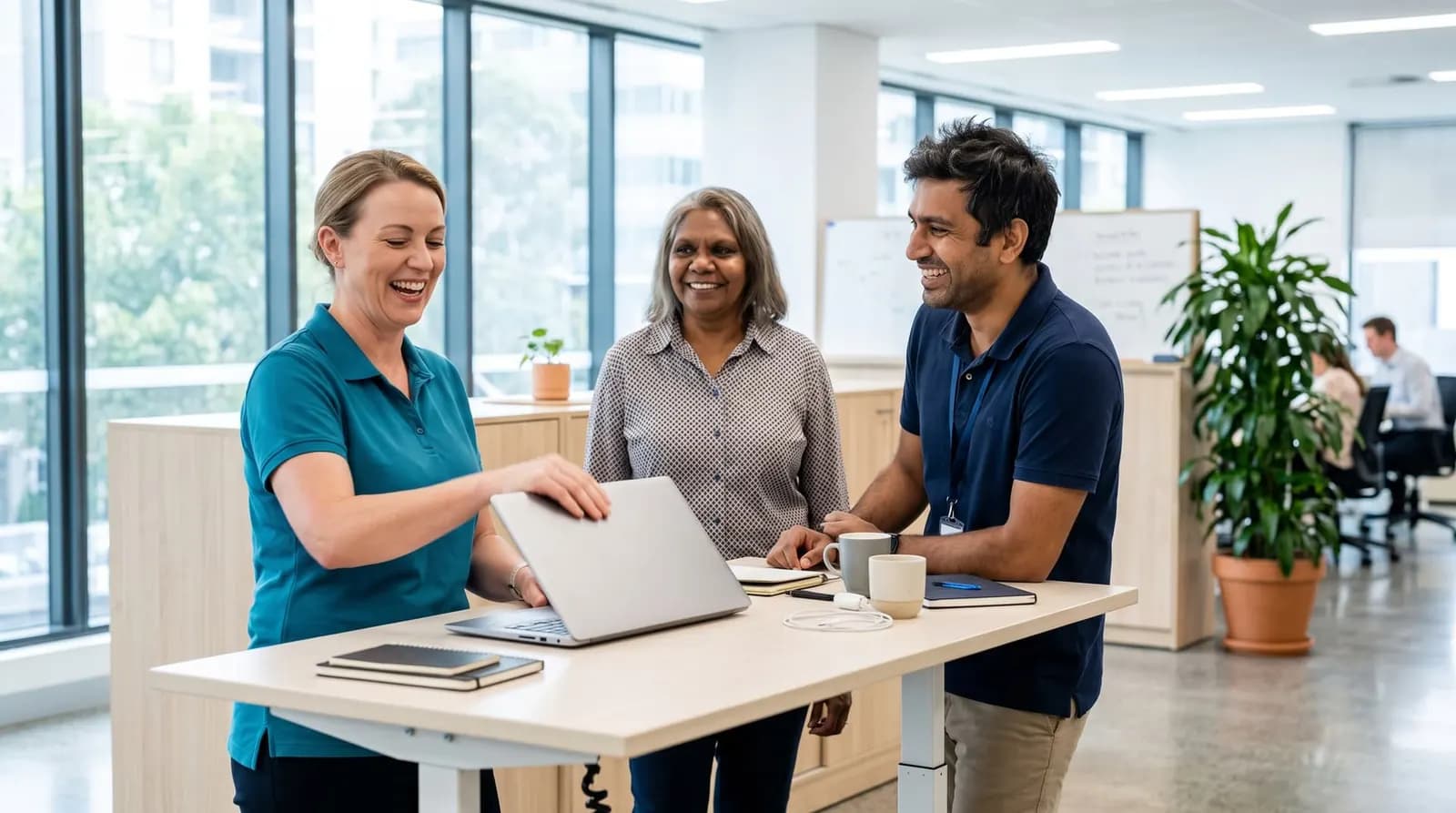 Three colleagues at a standing desk in a bright office, laughing together